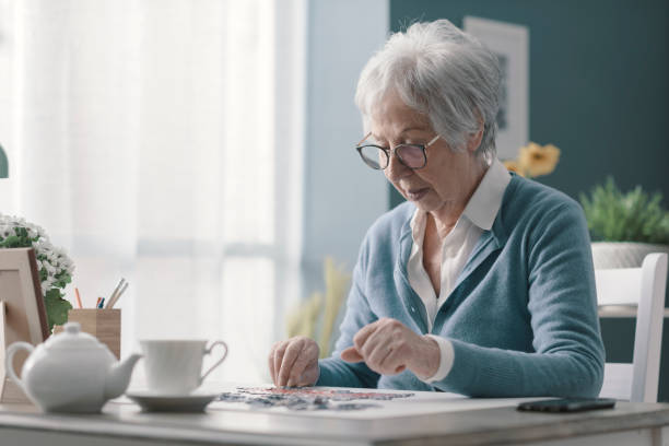 femme aîné s’asseyant au bureau et résolvant un puzzle - jeux mémoire photos et images de collection
